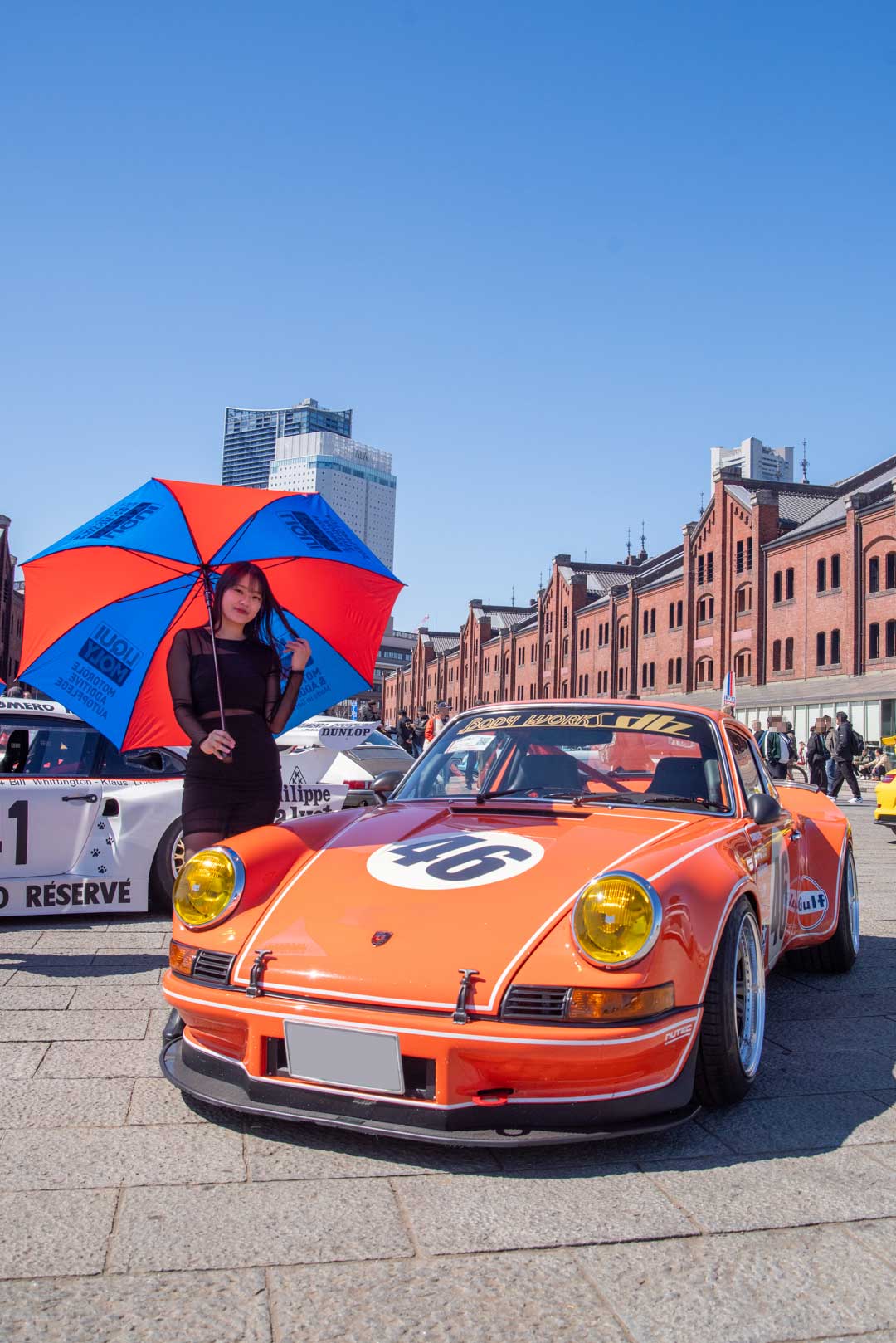 2026 年 EXCITING PORSCHE（横浜 赤レンガ倉庫）特別展示エリアの配置例 2。ゼッケン 46 のオレンジの 911 を正面から